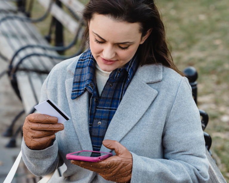 a woman on a park bench reads info about her credit card using a smart phone