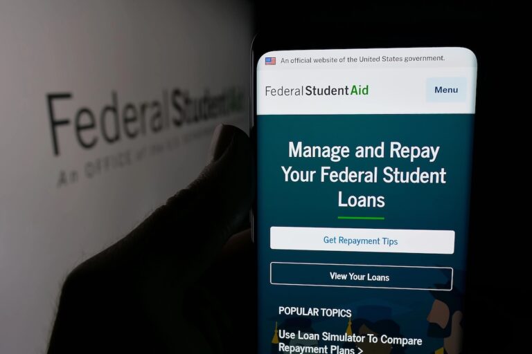 Person holding smartphone with web page of education office Federal Student Aid (FSA) on screen in front of logo. Focus on center of phone display.